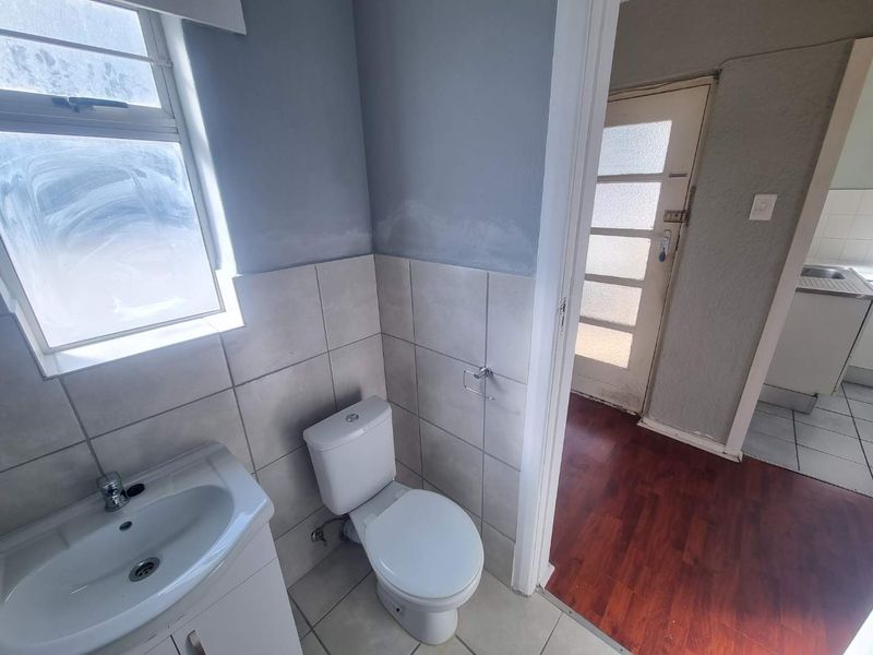 A compact bathroom featuring a pedestal basin, toilet, and tiled walls, requiring minor cosmetic updates to the paintwork and finishes.