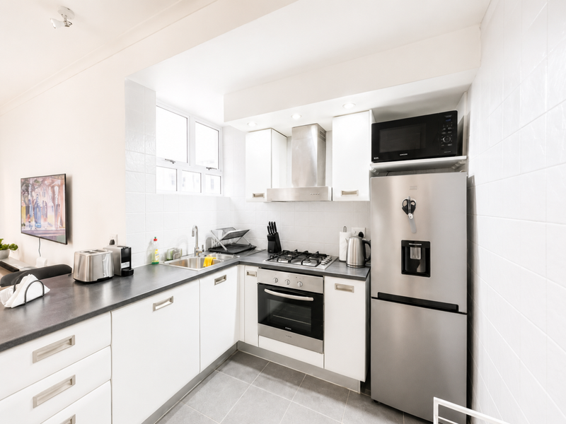 A clean, modern kitchen featuring white cabinetry, stainless steel appliances, a gas hob, built-in oven, and tiled splashbacks.