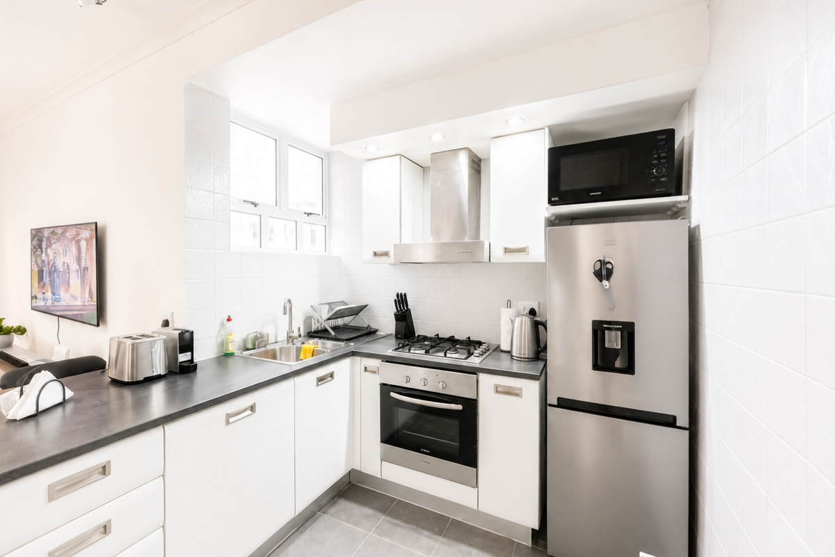 A clean, modern kitchen featuring white cabinetry, stainless steel appliances, a gas hob, built-in oven, and tiled splashbacks.