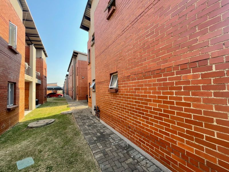 Exterior view of the apartment complex featuring exposed brick facades, a paved walkway, and shared lawn area between building blocks.