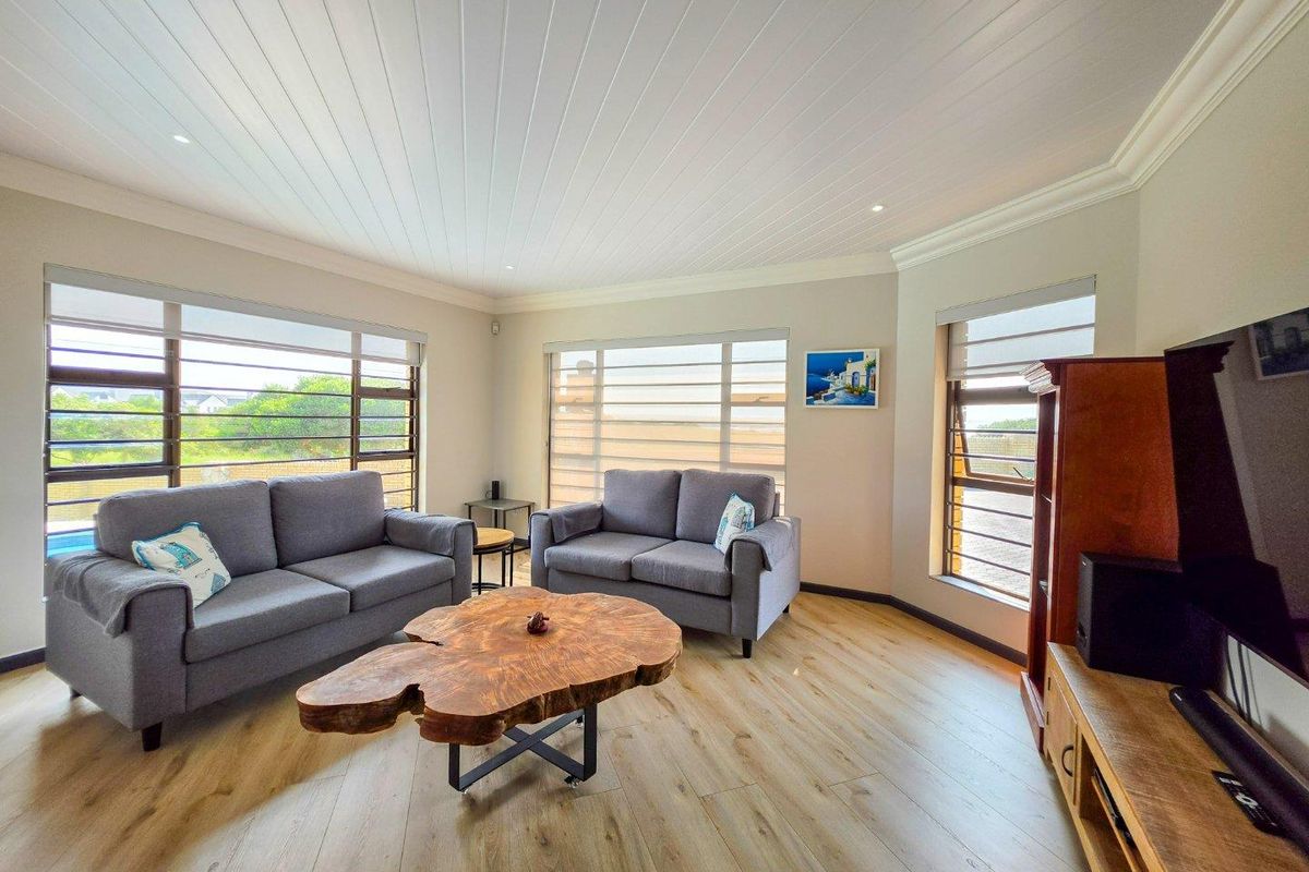 A bright and modern living room featuring light wood-look laminate flooring, a white tongue and groove ceiling, and large windows with roller blinds.