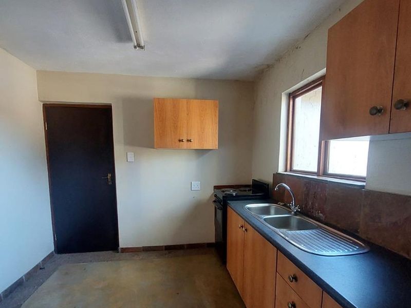 A functional kitchen area featuring wooden cabinetry, a stainless steel double sink, and a freestanding stove, requiring cosmetic updates.