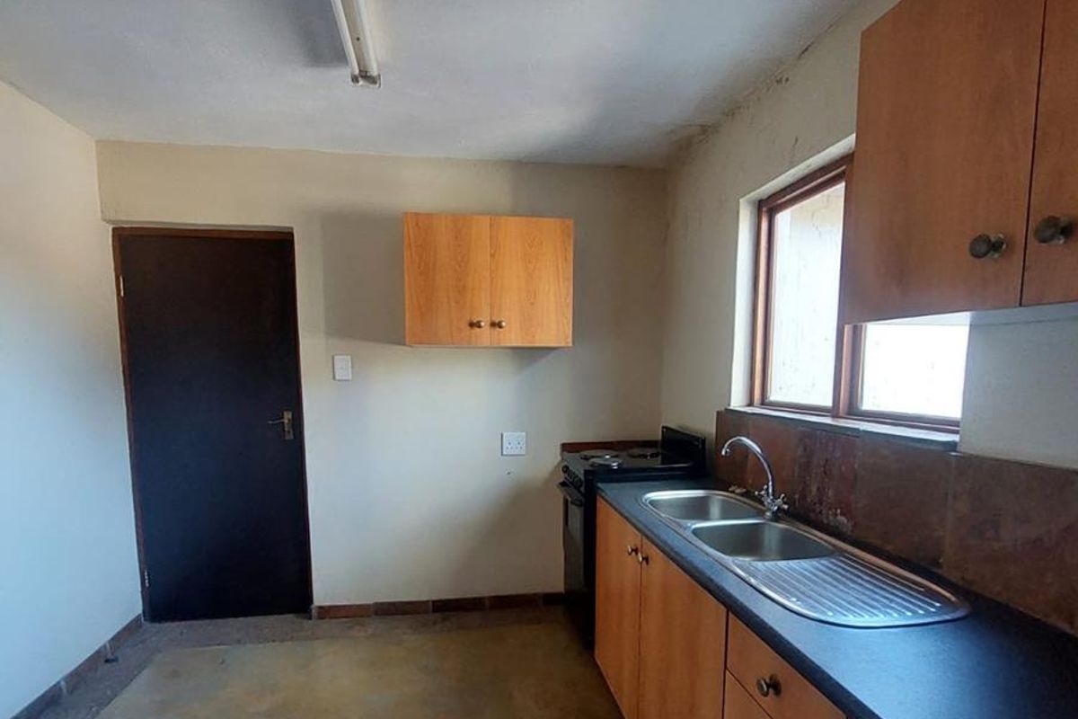 A functional kitchen area featuring wooden cabinetry, a stainless steel double sink, and a freestanding stove, requiring cosmetic updates.