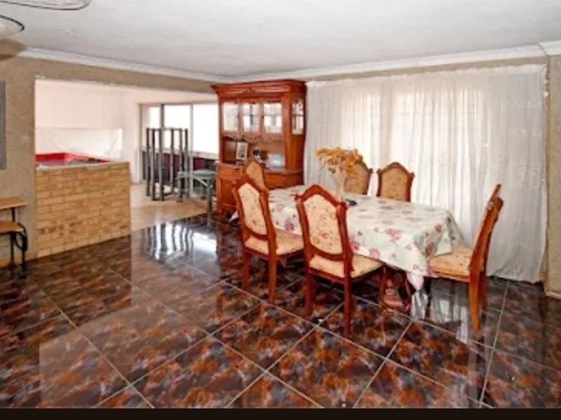 Open plan living and dining area featuring dark patterned floor tiles and a brick partition wall, offering a dated interior space ready for modernization.
