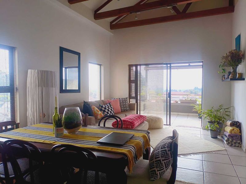 Spacious open-plan living and dining area featuring high vaulted ceilings with exposed timber beams, tiled floors, and large sliding doors leading to a balcony.