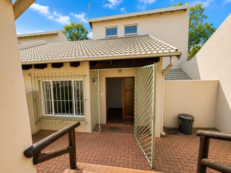 Rear exterior view of the apartment featuring a paved patio area, security gate, and protective window bars.