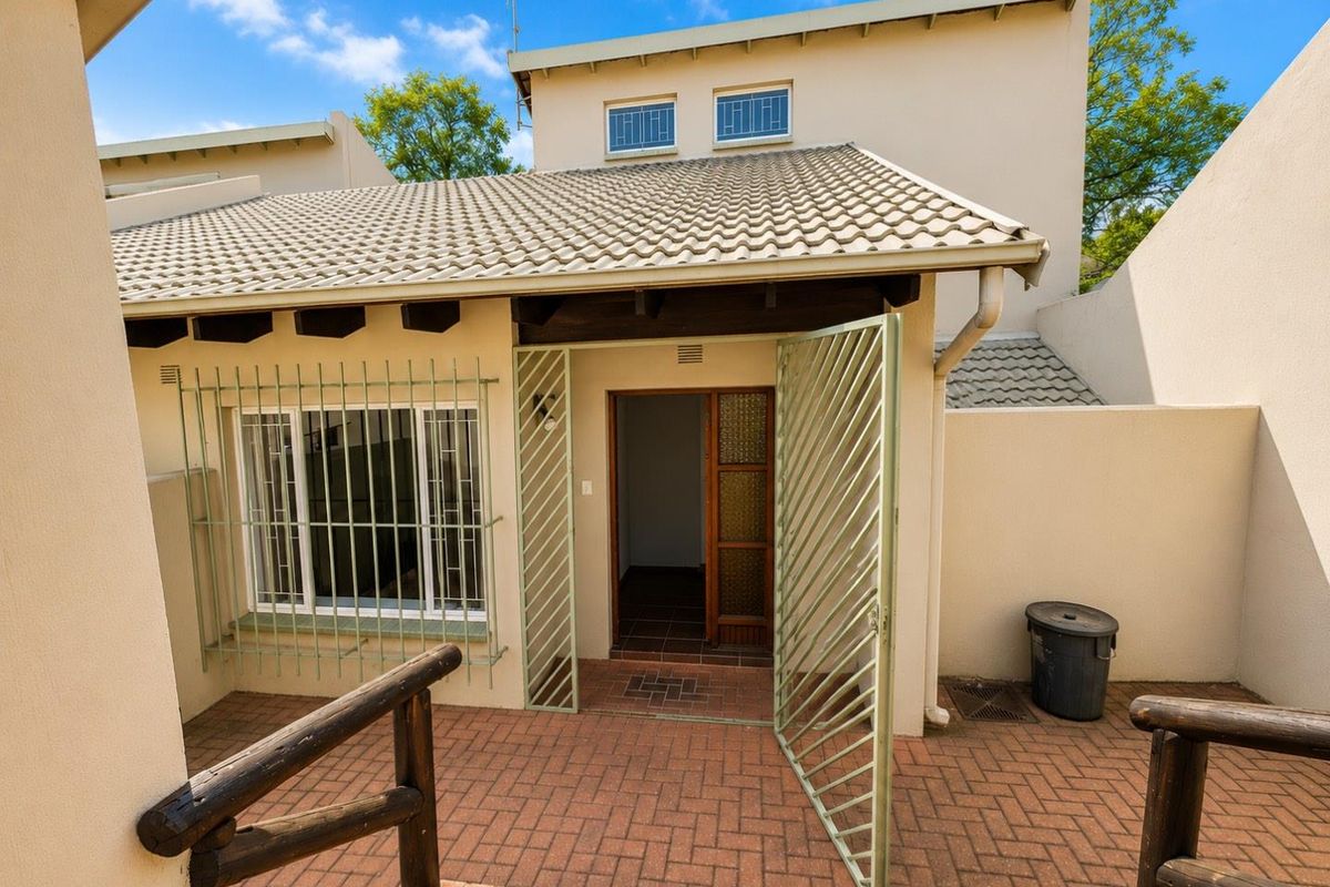 Rear exterior view of the apartment featuring a paved patio area, security gate, and protective window bars.