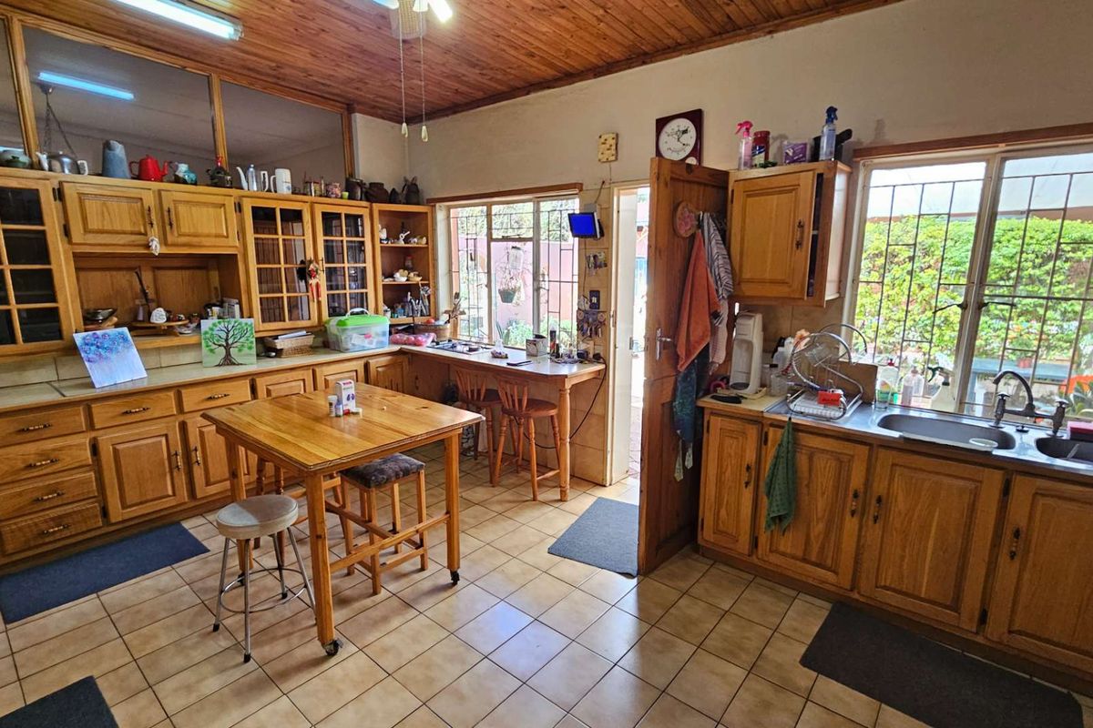 A rustic kitchen featuring extensive wooden cabinetry, tiled flooring, a breakfast nook, and large windows providing natural light and garden views.