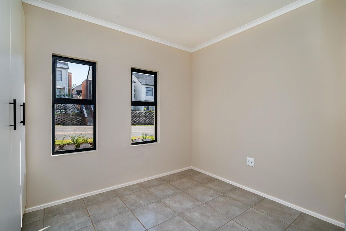 A bright, empty bedroom featuring neutral tiled flooring, built-in cabinetry, and modern black-framed windows overlooking the street.