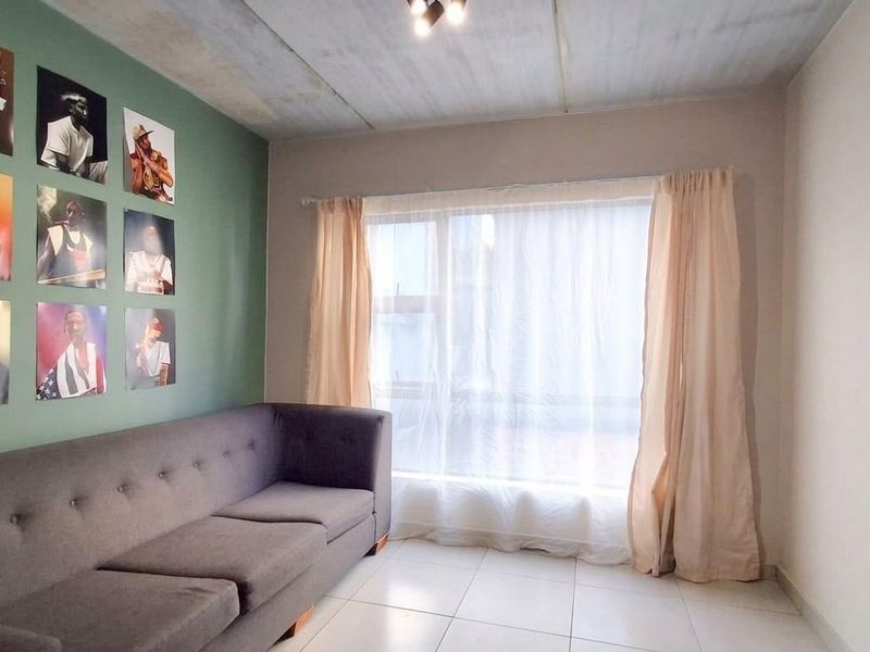 A living room featuring tiled flooring, a large window with curtains, and a painted accent wall.