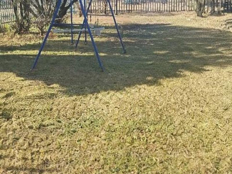 A spacious backyard area featuring a grass lawn, mature trees, and secure metal perimeter fencing.