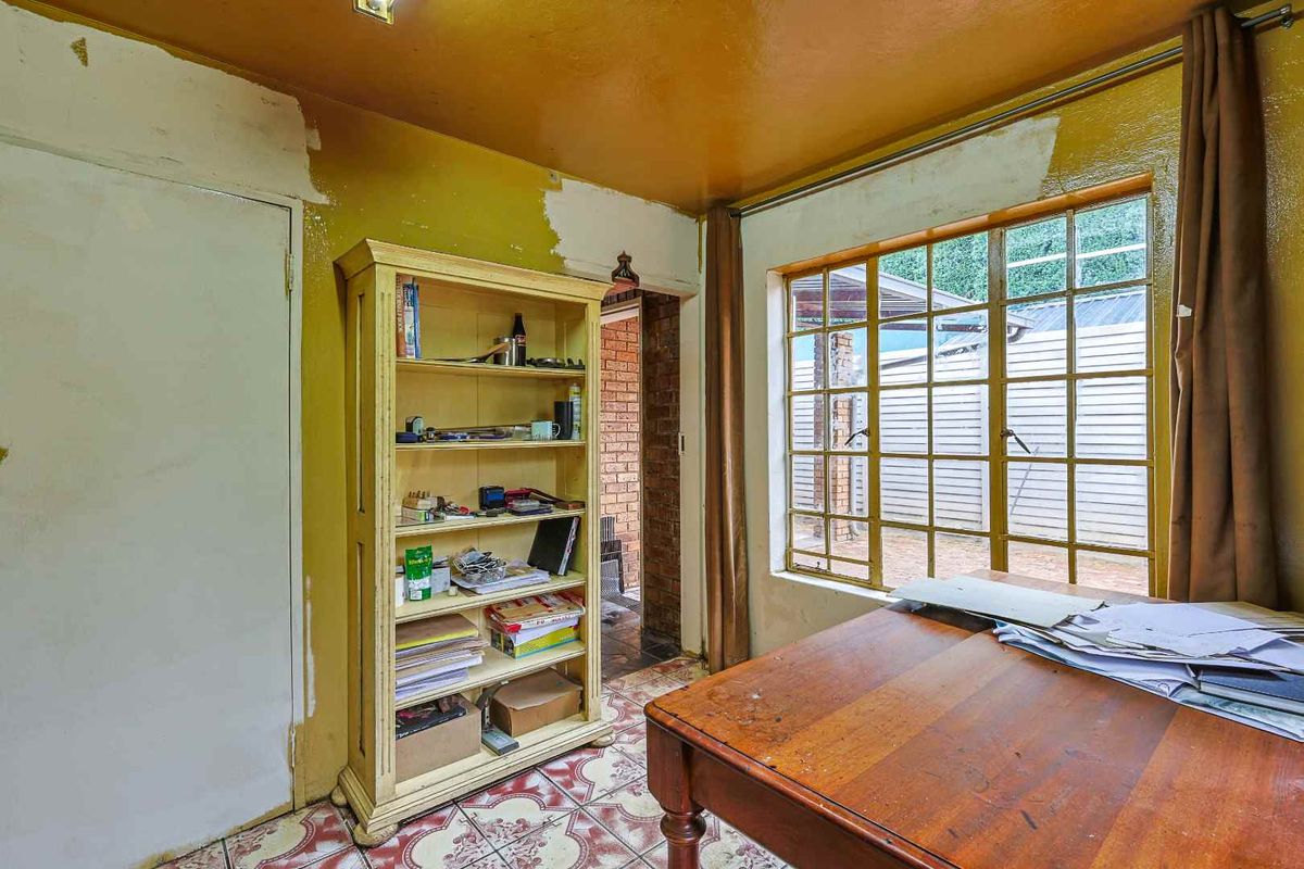 A dated room featuring original patterned floor tiles, large steel-framed windows, and walls requiring plastering and painting, offering potential for renovation.