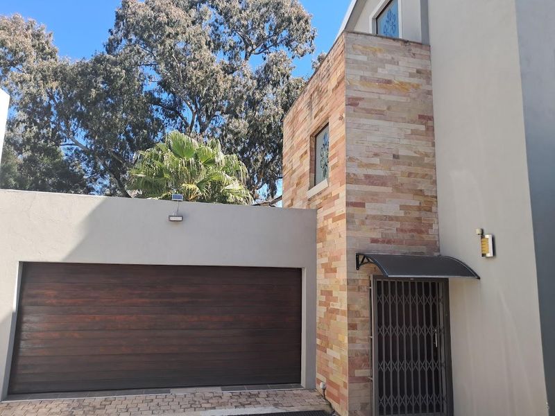 Front elevation of the townhouse featuring a modern sectional garage door, decorative stone cladding, and a secure entrance with an awning.