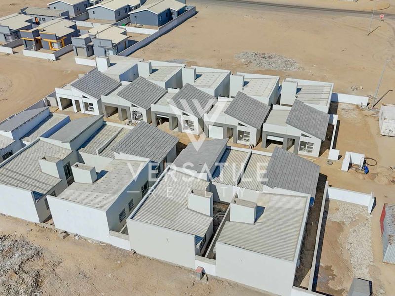 Aerial view of a modern townhouse development complex featuring pitched metal roofs and concrete boundary walls in a developing residential area.