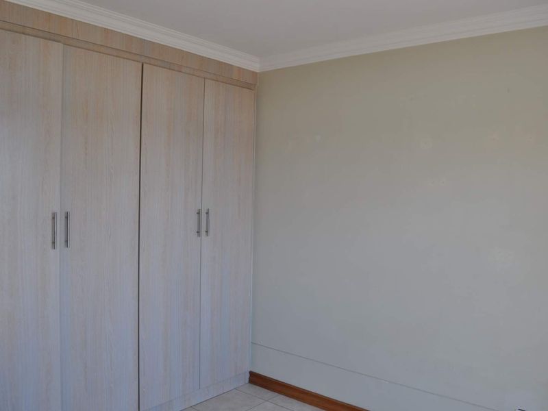 A clean, empty bedroom featuring light wood-finish built-in cupboards, crown molding, and neutral wall tones with tiled flooring.