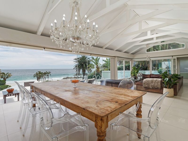 Spacious open-plan living and dining area featuring vaulted ceilings with exposed rafters, large format floor tiles, and expansive glass doors offering panoramic ocean views.