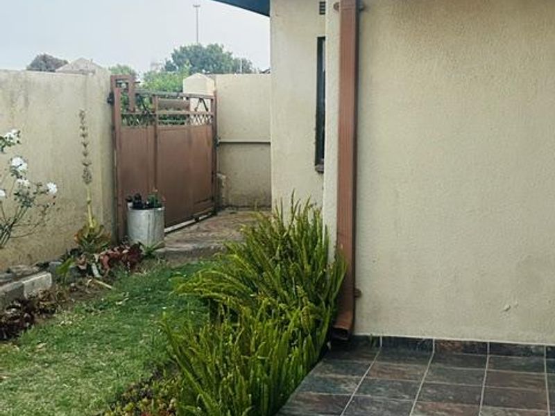 A view of the rear exterior featuring a tiled patio area, boundary wall, and metal gate access.