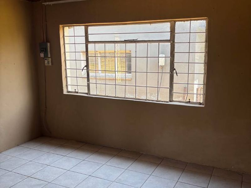 An empty bedroom featuring tiled flooring, a timber ceiling, and security burglar bars on the window.