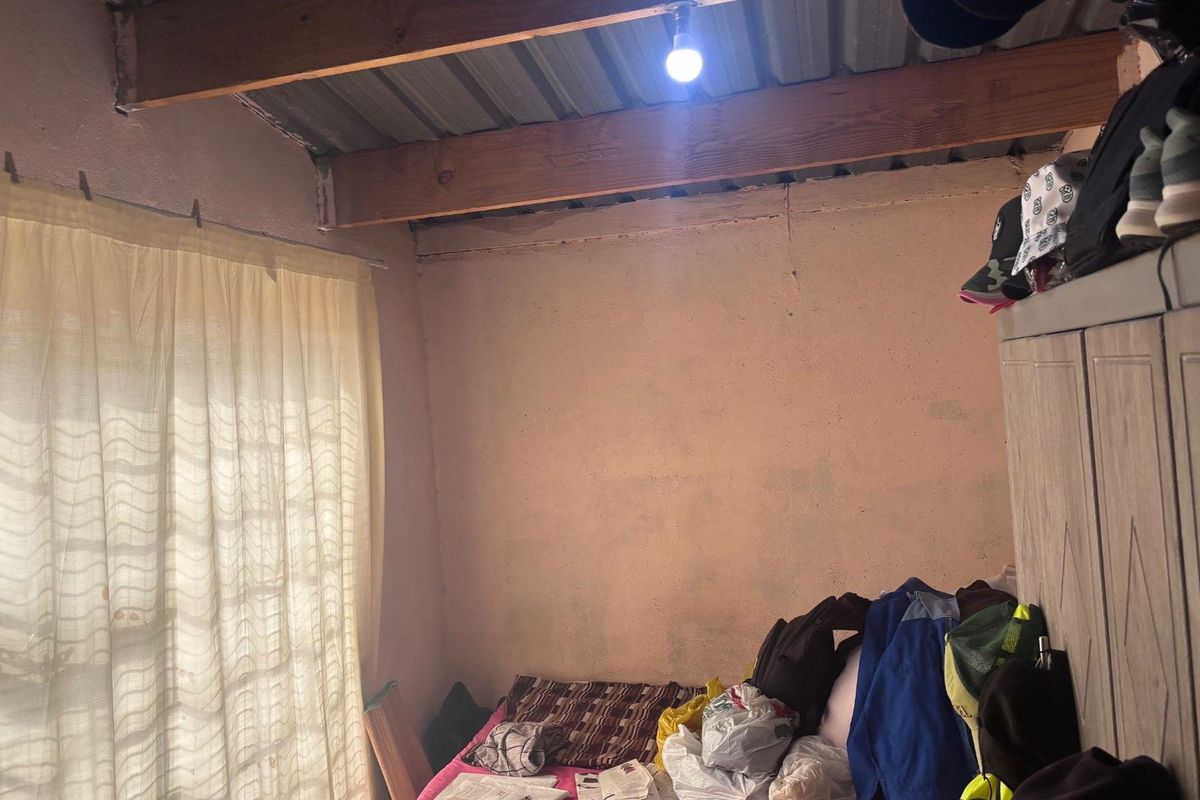 A bedroom featuring exposed timber beams and a corrugated metal ceiling, requiring cosmetic updates and finishing to improve the overall condition.
