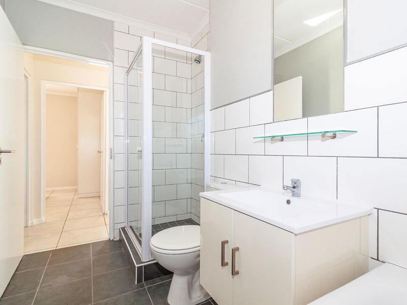 A clean, modern bathroom featuring a glass shower enclosure, vanity with basin, wall-mounted mirror, and contemporary subway tile finishes.