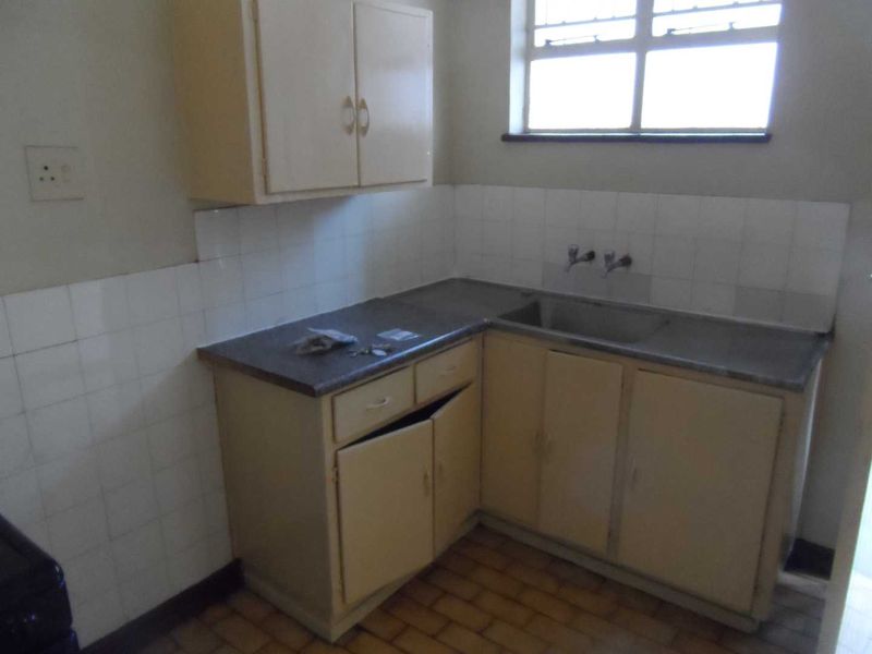 A compact, dated kitchen featuring original cabinetry, a stainless steel sink, and tiled splashbacks, offering potential for a modern renovation.