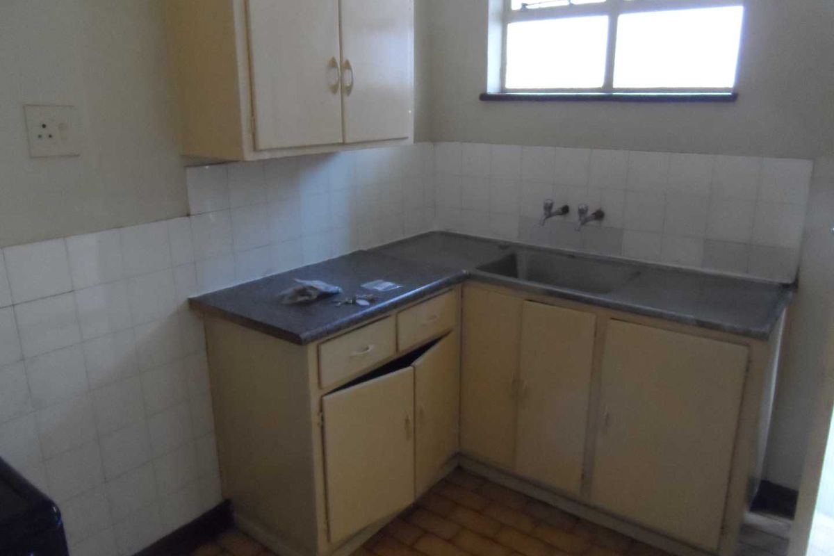 A compact, dated kitchen featuring original cabinetry, a stainless steel sink, and tiled splashbacks, offering potential for a modern renovation.