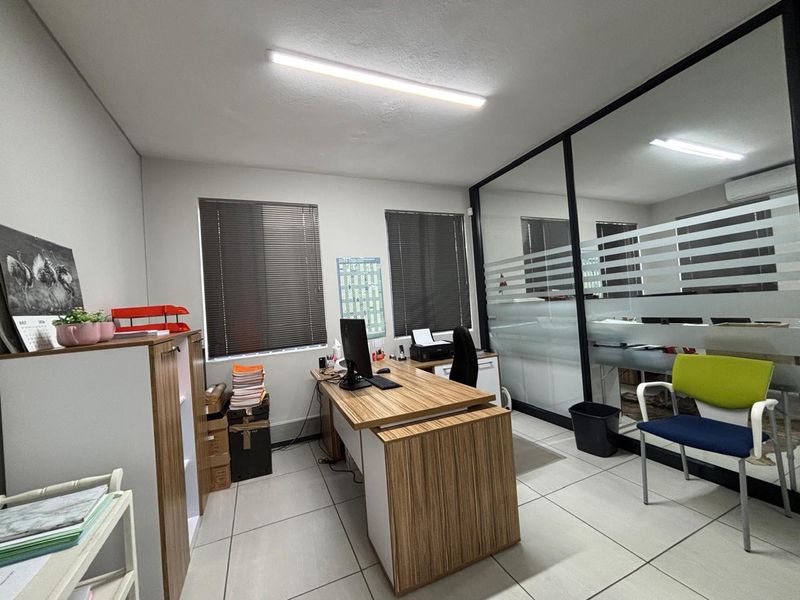 A functional office space featuring tiled flooring, aluminium-framed glass partitioning with privacy film, and venetian blinds for light control.