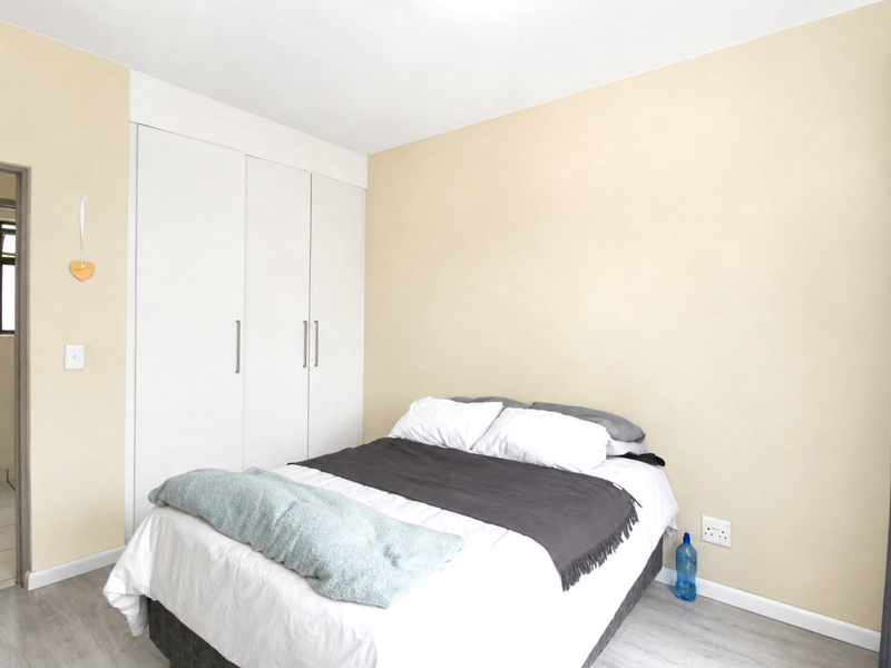 A well-maintained bedroom featuring neutral walls, light laminate flooring, and ample built-in cupboard storage with direct access to an adjacent bathroom.