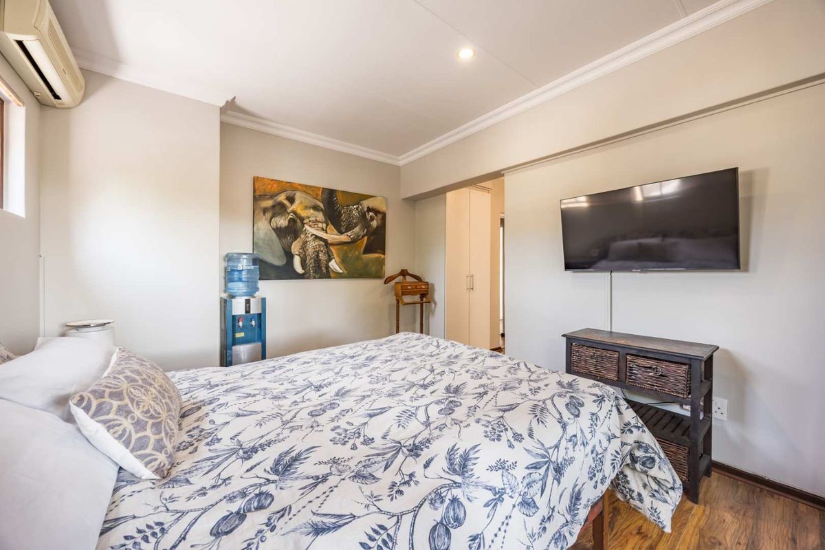 A well-maintained bedroom featuring laminate flooring, crown molding, a built-in wardrobe, and a wall-mounted air conditioning unit.