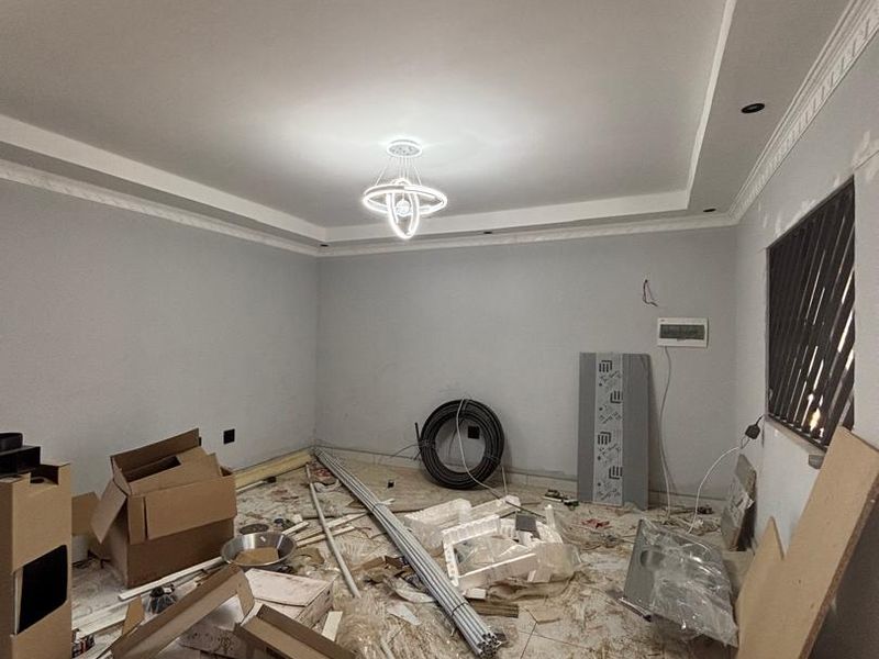 An unfinished living room space featuring crown molding, a modern chandelier, and tiled flooring, currently undergoing renovation with construction materials present.