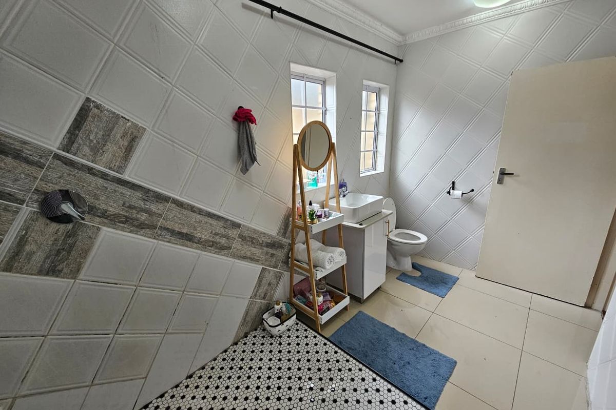 A functional bathroom featuring a walk-in shower with mosaic floor tiling, a vanity basin, and a toilet, finished with diamond-patterned wall tiles.