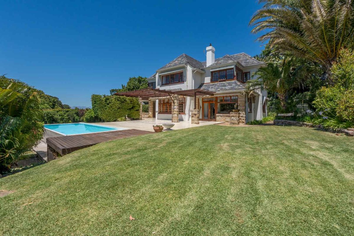 Rear view of a multi-story residence featuring a swimming pool, timber deck, pergola, and landscaped garden area.