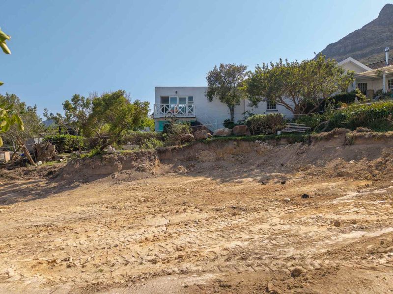 A view of a vacant residential plot featuring an exposed soil embankment and established garden area with a neighboring property in the background.