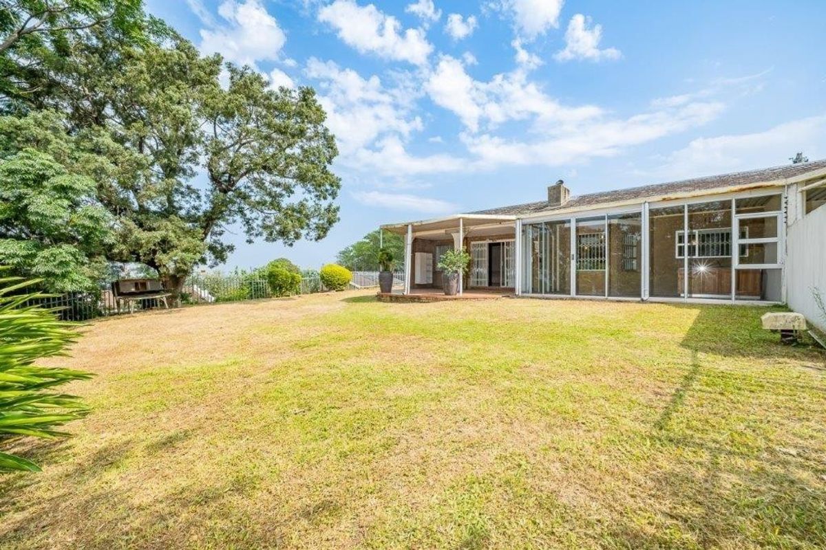 Spacious rear garden featuring a covered patio area and an enclosed sunroom with large windows, offering potential for outdoor living and entertainment.