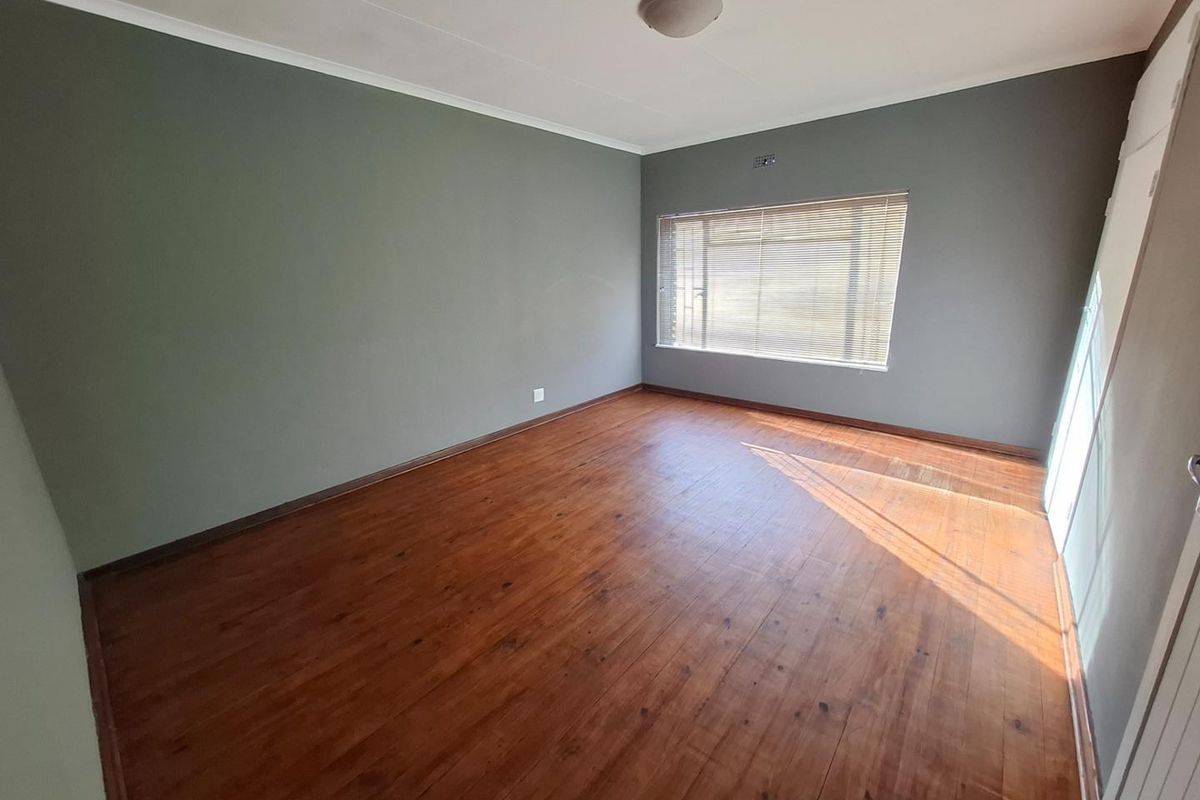 A spacious, empty bedroom featuring warm timber flooring, neutral grey walls, and fitted venetian blinds, offering a clean canvas for personalization.