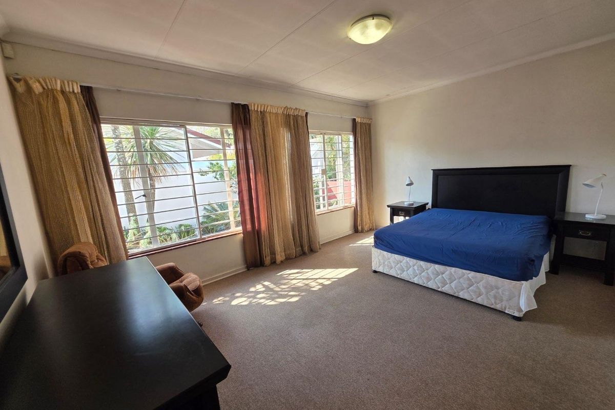 Spacious bedroom featuring large windows with security bars, neutral carpeting, and ample natural light.