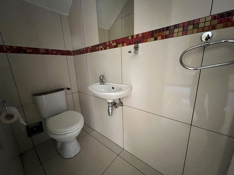 A compact guest bathroom featuring a wall-mounted basin, toilet, and neutral wall tiles with a decorative mosaic border.
