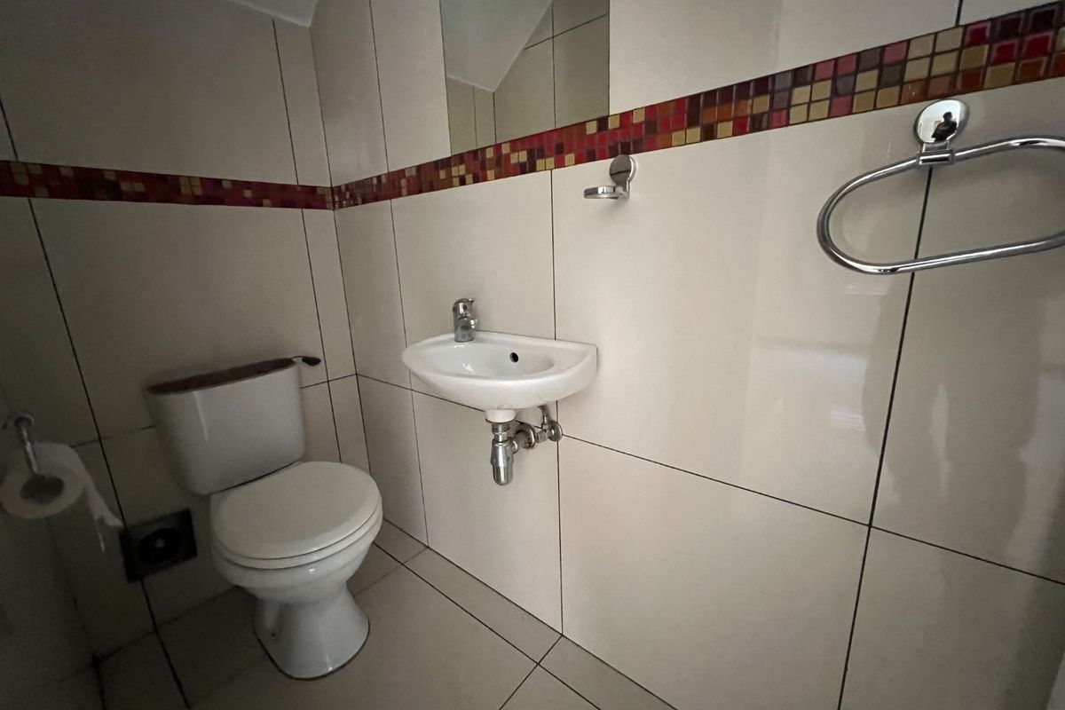 A compact guest bathroom featuring a wall-mounted basin, toilet, and neutral wall tiles with a decorative mosaic border.