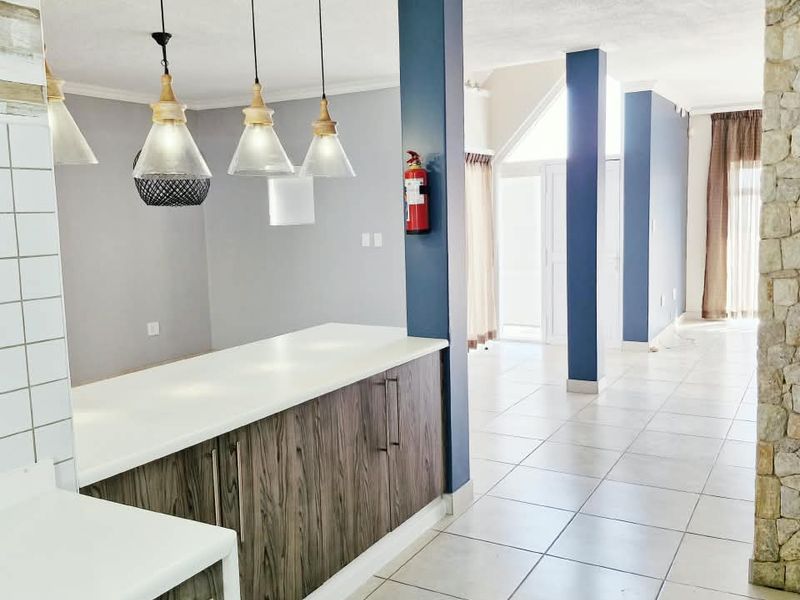 Open plan living area featuring modern kitchen cabinetry, stone veneer accents, ceramic tile flooring, and structural columns with integrated pendant lighting.
