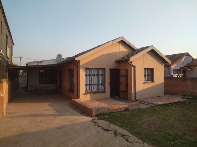 A single-story residential property featuring a tiled roof, security bars on windows, a concrete driveway, and an attached carport.