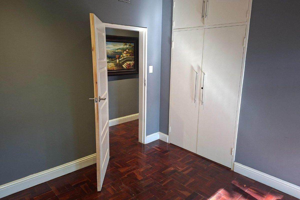 A clean bedroom featuring polished parquet flooring, built-in storage cupboards, and a neutral grey wall finish with white trim.
