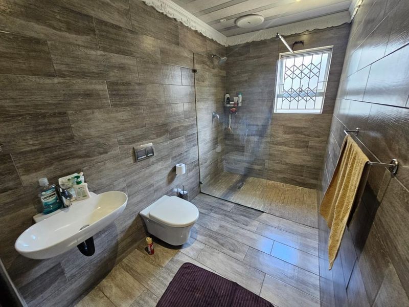 Modern bathroom featuring wood-look tiled walls and floors, a wall-hung toilet, a wall-mounted basin, and a spacious walk-in shower with a glass screen.