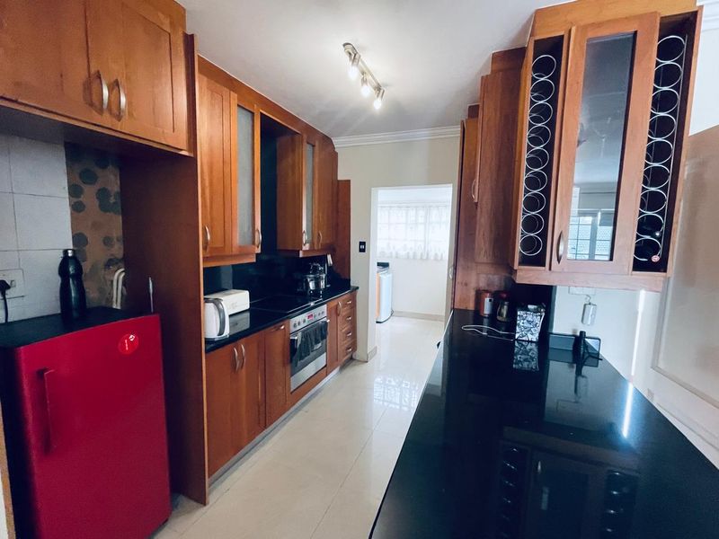 A functional kitchen featuring warm-toned wooden cabinetry, sleek black granite countertops, built-in oven, and tiled flooring, offering ample storage and workspace.