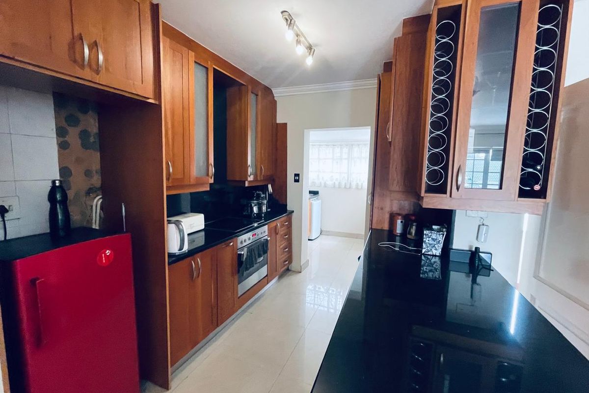 A functional kitchen featuring warm-toned wooden cabinetry, sleek black granite countertops, built-in oven, and tiled flooring, offering ample storage and workspace.