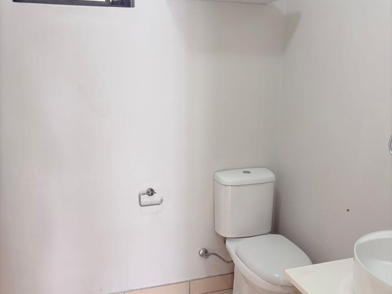 A clean and functional bathroom featuring a modern vanity with basin, a standard toilet, and a louver window for ventilation.