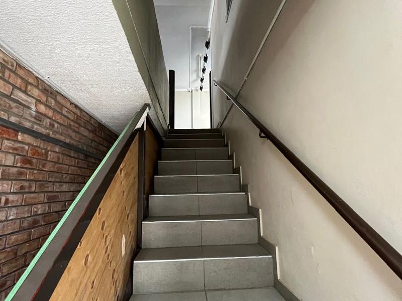 A functional interior staircase featuring tiled steps, a handrail, and an exposed brick wall section, currently showing signs of wear and unfinished plywood paneling.