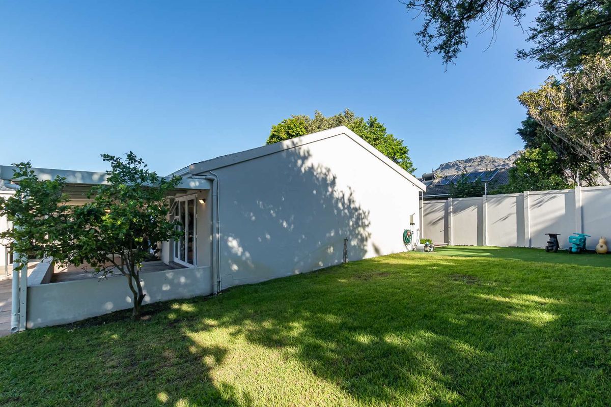 A view of the rear exterior of the house, featuring a well-maintained lawn, garden area, and a covered patio space.