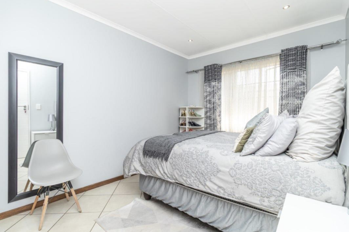A well-lit bedroom featuring tiled flooring, recessed ceiling lighting, and a large window with curtain tracks.