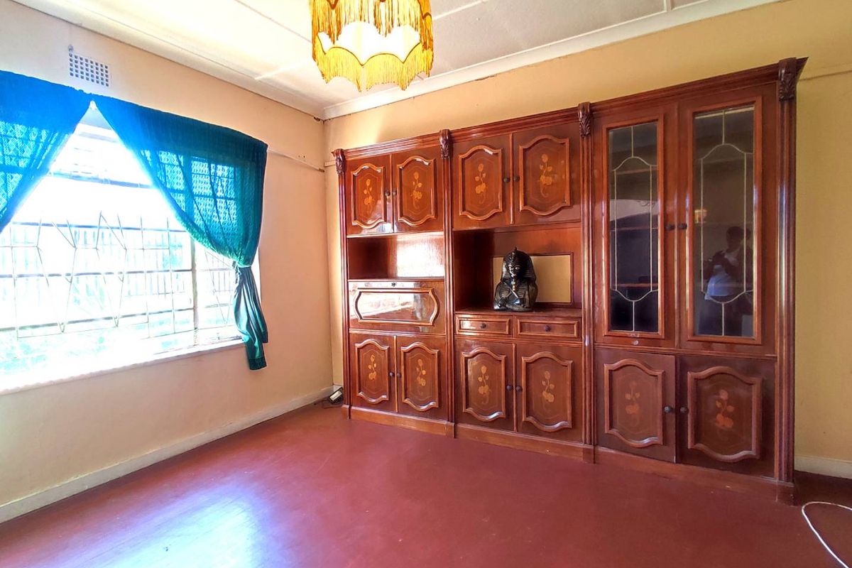 Living room featuring built-in wooden cabinetry, security bars on the window, and a coved ceiling. The space requires cosmetic updates to the flooring and finishes.