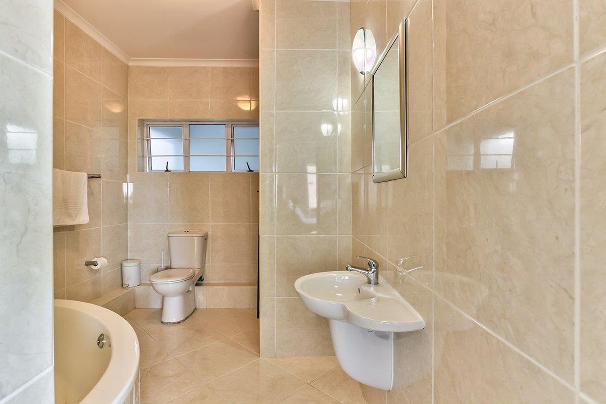 A clean, tiled bathroom featuring a pedestal basin, toilet, and built-in bathtub with neutral wall and floor finishes.